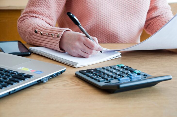 woman seated at a desk, focused on writing and using a calculator