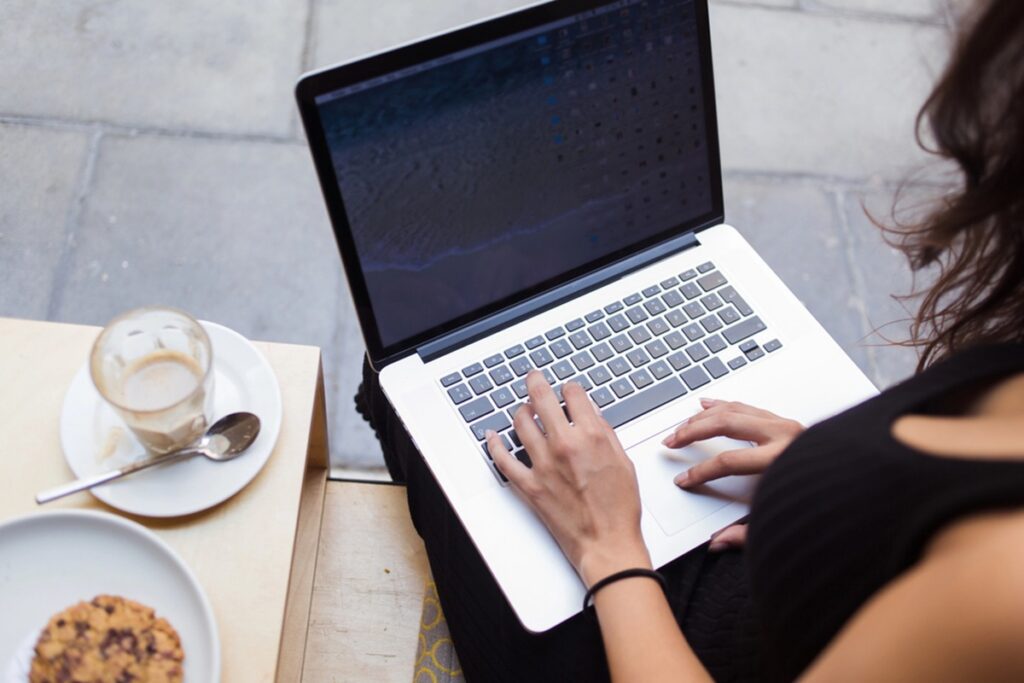 woman types on her laptop while seated on a bench, engaged in her work in a public space